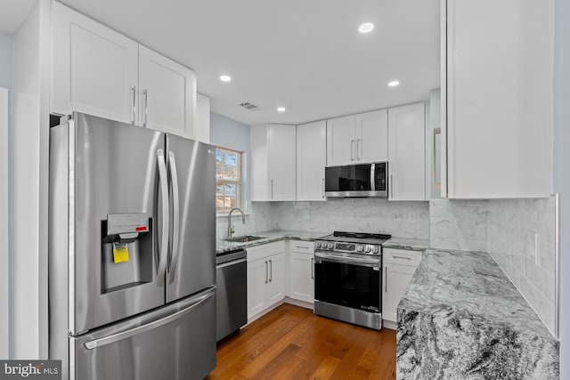 kitchen with white cabinetry, stainless steel appliances, sink, backsplash, and light stone counters