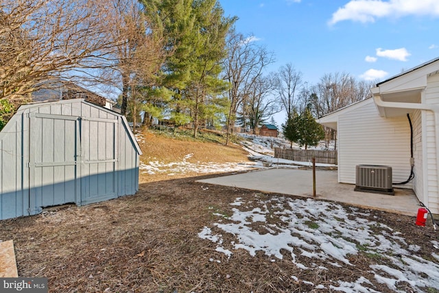 yard covered in snow with a patio area, central AC, and a storage unit