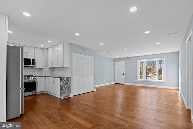 kitchen with hardwood / wood-style floors, white cabinetry, stainless steel appliances, backsplash, and light stone counters