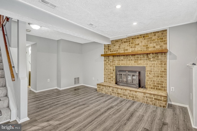 unfurnished living room with hardwood / wood-style flooring, a textured ceiling, a brick fireplace, and beamed ceiling