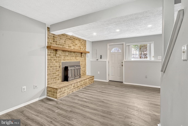 unfurnished living room with hardwood / wood-style flooring, a textured ceiling, and a brick fireplace