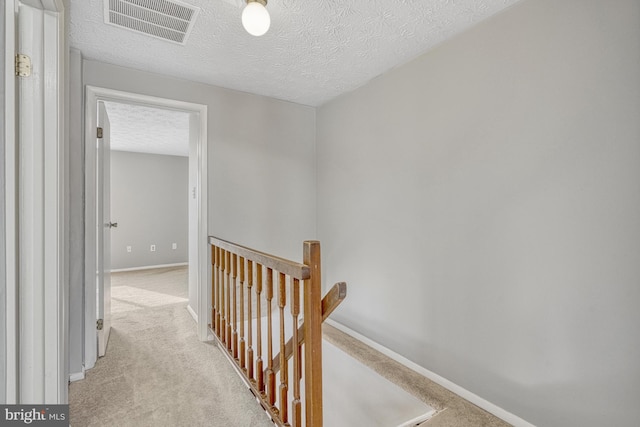 hallway with light carpet and a textured ceiling