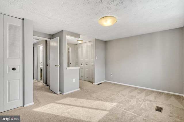 interior space featuring a textured ceiling, light carpet, and multiple closets