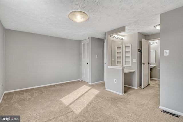 unfurnished bedroom with ensuite bath, a textured ceiling, and light carpet