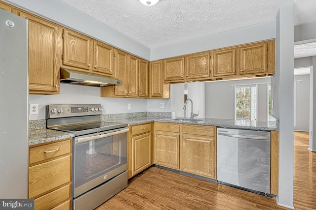 kitchen with appliances with stainless steel finishes, sink, light wood-type flooring, light stone counters, and a textured ceiling