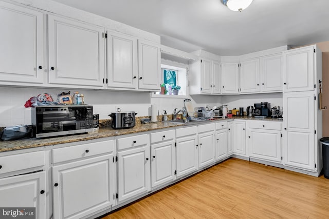 kitchen featuring dark stone countertops, sink, white cabinets, and light wood-type flooring