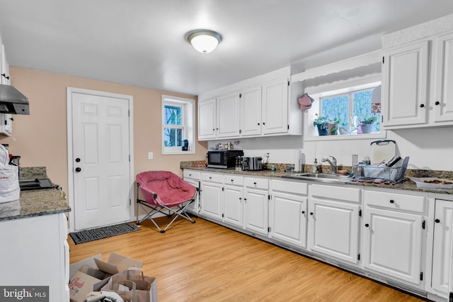 kitchen featuring white cabinets, dark stone counters, sink, and light hardwood / wood-style floors