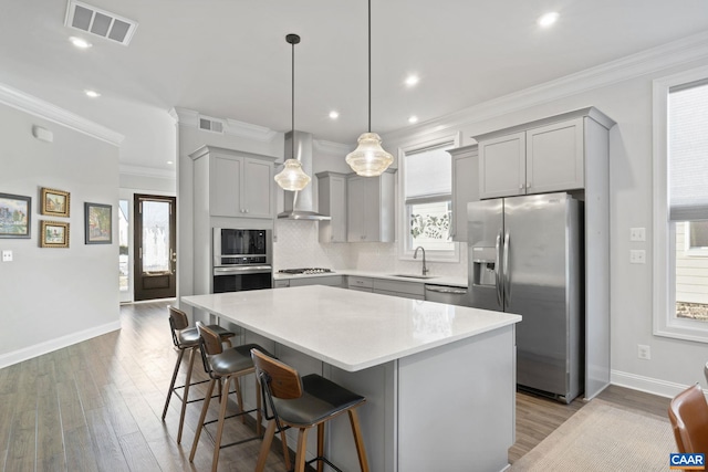 kitchen featuring appliances with stainless steel finishes, wall chimney exhaust hood, a kitchen island, decorative light fixtures, and sink