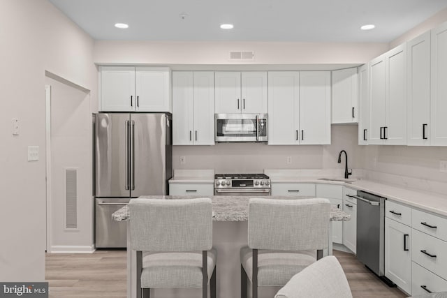 kitchen featuring sink, light stone countertops, a kitchen breakfast bar, appliances with stainless steel finishes, and white cabinets