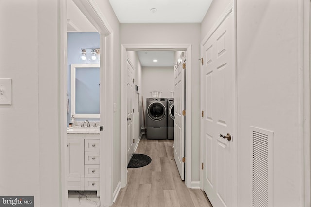 hallway with sink, washing machine and clothes dryer, and light hardwood / wood-style flooring