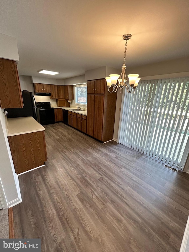 kitchen featuring dark hardwood / wood-style floors, black appliances, sink, hanging light fixtures, and a chandelier