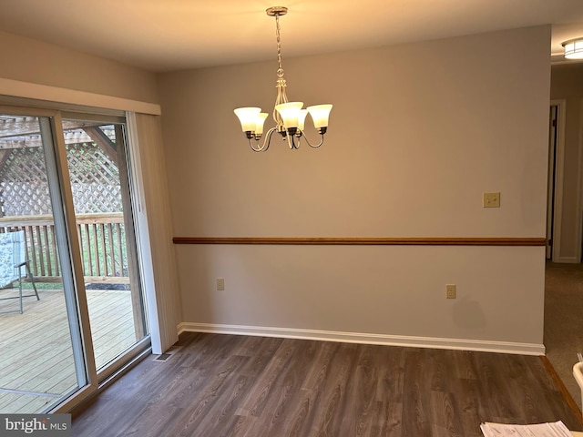 unfurnished dining area featuring dark wood-type flooring and an inviting chandelier