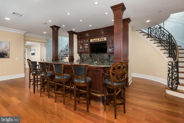 bar with tasteful backsplash, dark wood-type flooring, ornamental molding, and ornate columns