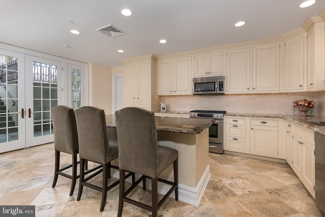 kitchen with stainless steel appliances, cream cabinetry, french doors, and dark stone counters