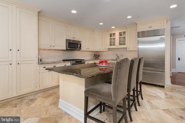 kitchen featuring a breakfast bar, stainless steel appliances, cream cabinets, and dark stone countertops