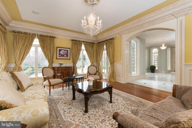 sitting room with an inviting chandelier, a wealth of natural light, crown molding, and hardwood / wood-style flooring