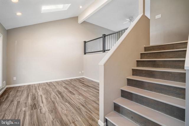 stairs featuring ceiling fan, wood-type flooring, and lofted ceiling with skylight