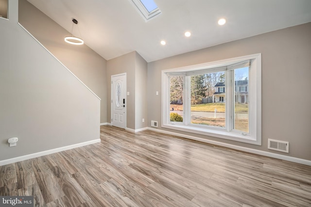 unfurnished living room featuring lofted ceiling with skylight and light hardwood / wood-style flooring