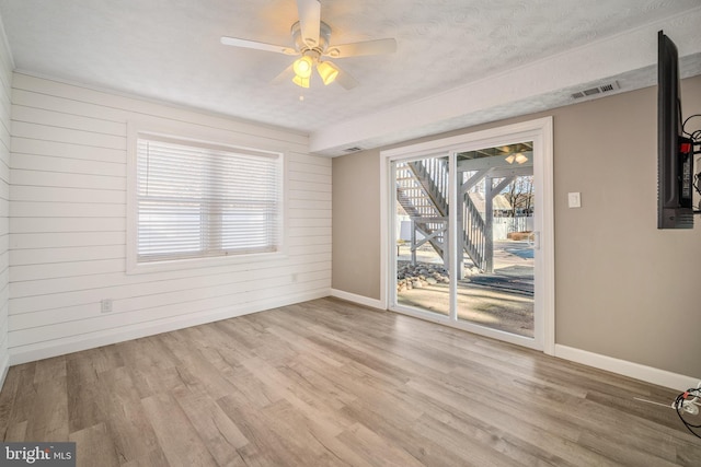 empty room featuring light hardwood / wood-style floors, a textured ceiling, ceiling fan, and wooden walls