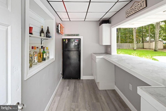 interior space featuring black fridge, a paneled ceiling, white cabinetry, and hardwood / wood-style floors