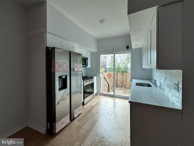 kitchen featuring white cabinetry, appliances with stainless steel finishes, light hardwood / wood-style flooring, light stone counters, and sink