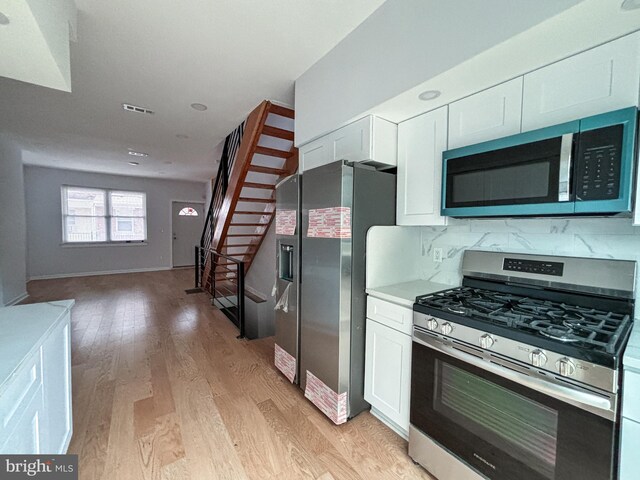 kitchen with tasteful backsplash, white cabinets, light wood-type flooring, and appliances with stainless steel finishes