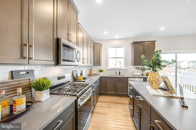 kitchen featuring tasteful backsplash, light hardwood / wood-style floors, sink, appliances with stainless steel finishes, and light stone counters