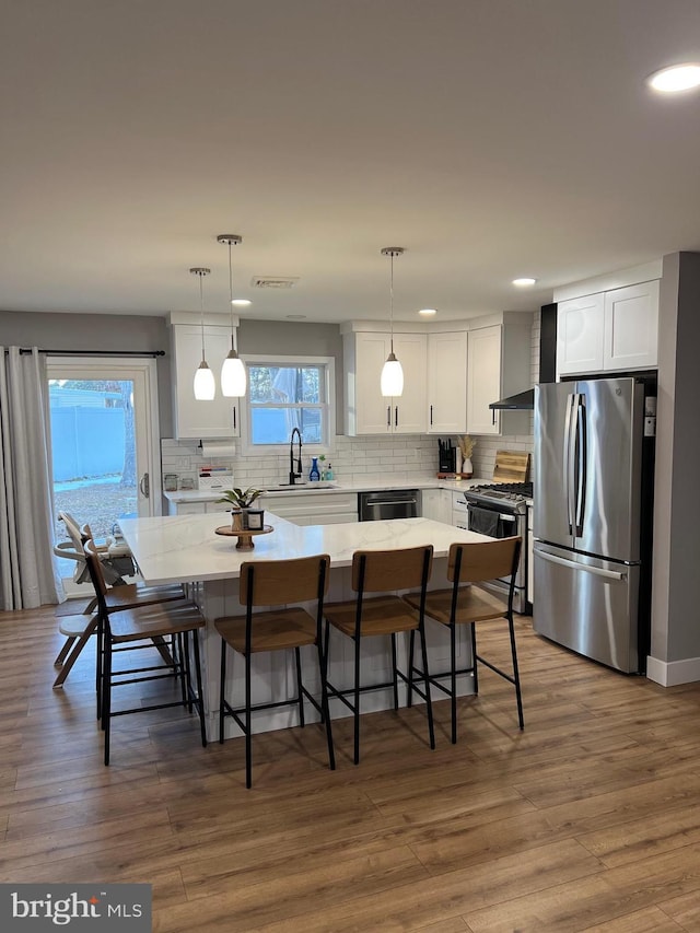 kitchen featuring decorative light fixtures, white cabinets, appliances with stainless steel finishes, and a center island