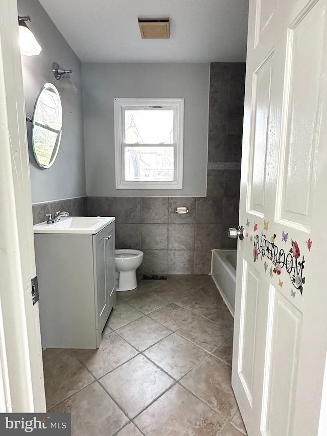 bathroom with tile patterned floors, toilet, tile walls, vanity, and a bathtub