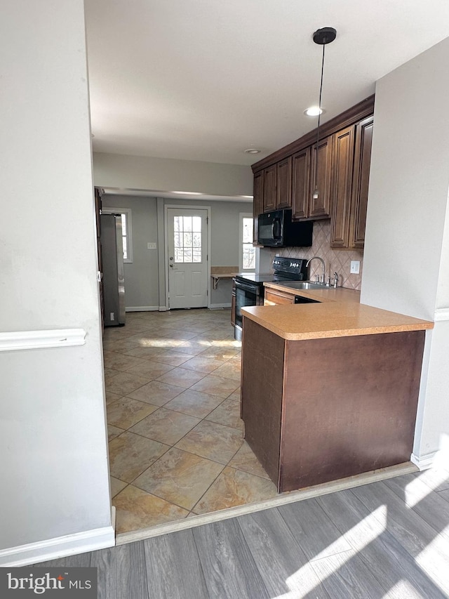 kitchen featuring pendant lighting, black appliances, sink, backsplash, and kitchen peninsula