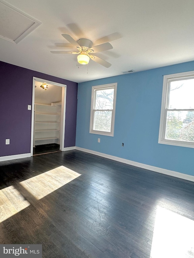 empty room with dark wood-type flooring, plenty of natural light, and ceiling fan