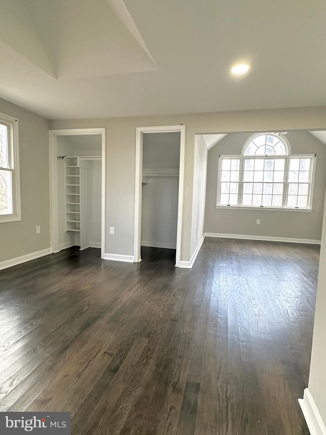 unfurnished bedroom featuring multiple windows, vaulted ceiling, dark hardwood / wood-style floors, and multiple closets