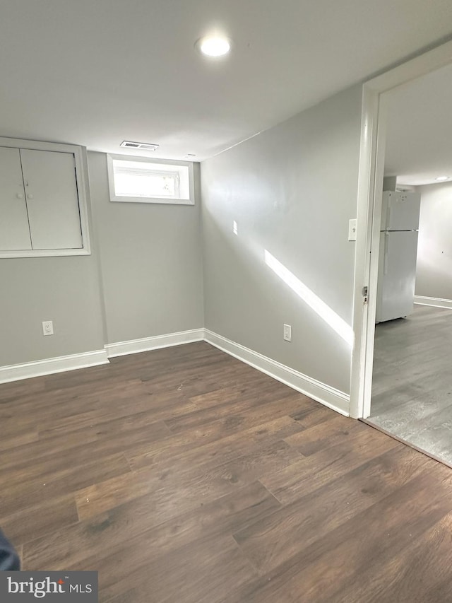 basement with white refrigerator and dark wood-type flooring