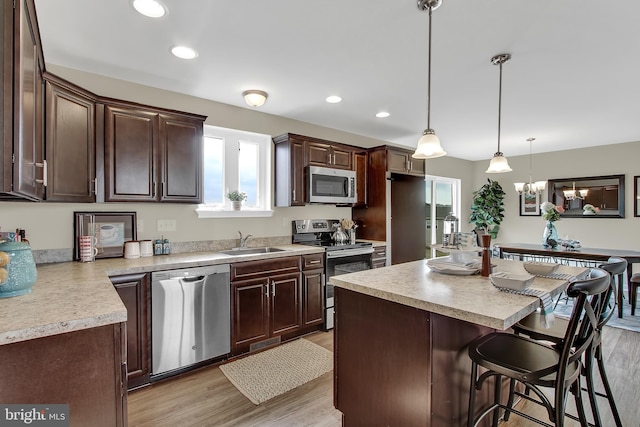 kitchen with appliances with stainless steel finishes, dark brown cabinets, a kitchen island, and pendant lighting