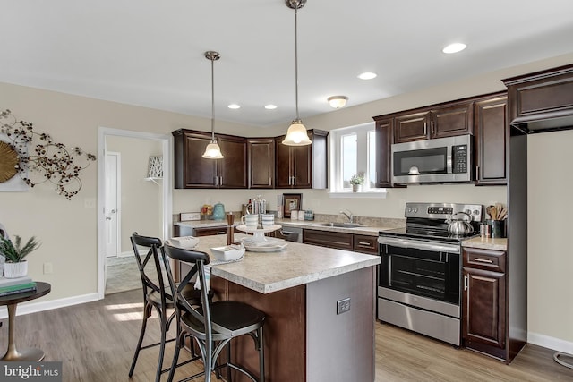 kitchen with decorative light fixtures, a center island, sink, light hardwood / wood-style flooring, and appliances with stainless steel finishes