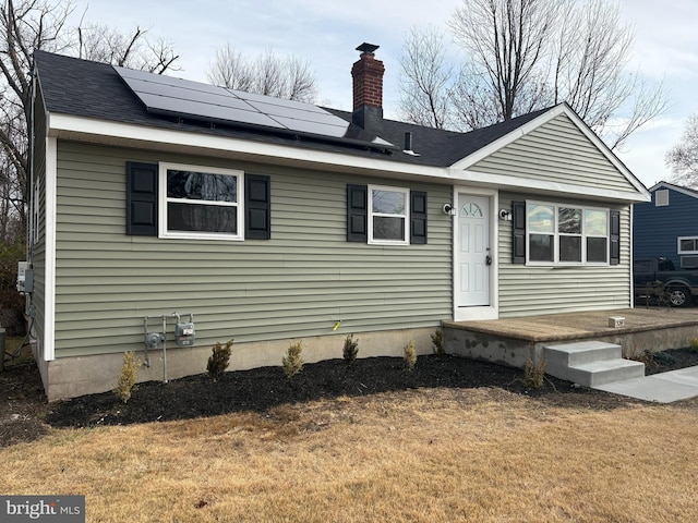 view of front of home featuring a front yard, solar panels, a chimney, and roof with shingles