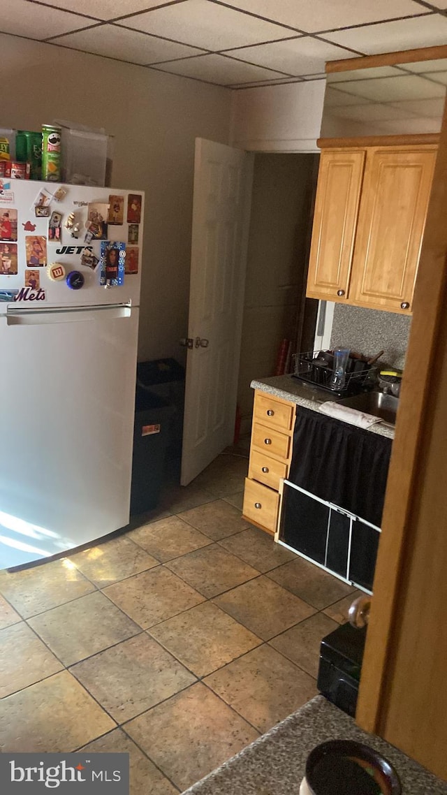 kitchen with sink, light brown cabinets, white refrigerator, and a drop ceiling