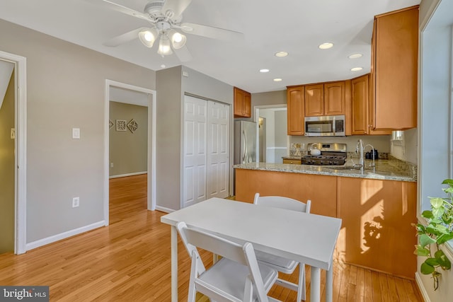 kitchen featuring ceiling fan, light hardwood / wood-style floors, kitchen peninsula, stainless steel appliances, and light stone counters