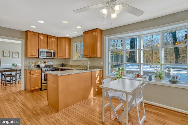 kitchen featuring light stone countertops, stainless steel appliances, light hardwood / wood-style floors, kitchen peninsula, and ceiling fan