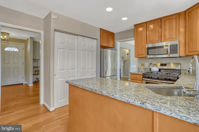 kitchen featuring light stone countertops, appliances with stainless steel finishes, sink, and light wood-type flooring