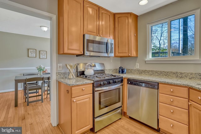 kitchen with stainless steel appliances, light hardwood / wood-style floors, and light stone countertops