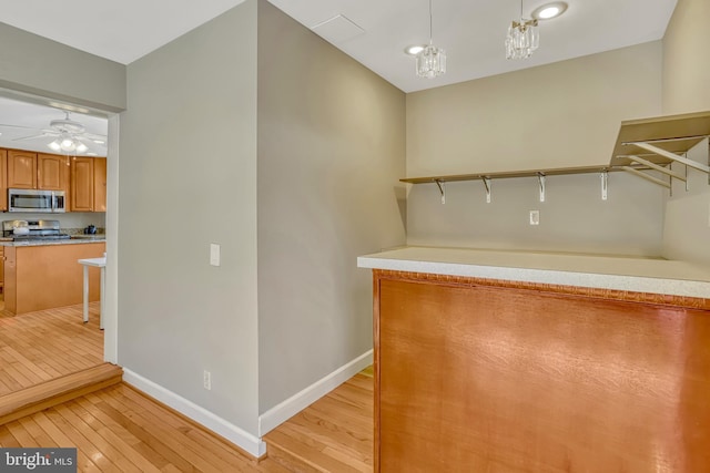 walk in closet with ceiling fan with notable chandelier and light wood-type flooring