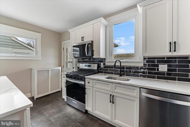 kitchen with white cabinetry, appliances with stainless steel finishes, radiator, light stone counters, and sink