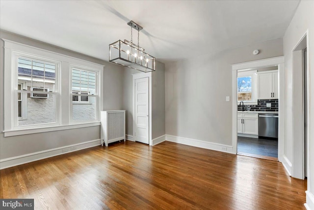 unfurnished dining area with a chandelier, sink, wood-type flooring, and radiator heating unit