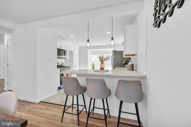 kitchen featuring backsplash, a breakfast bar, white cabinetry, light wood-type flooring, and stainless steel appliances