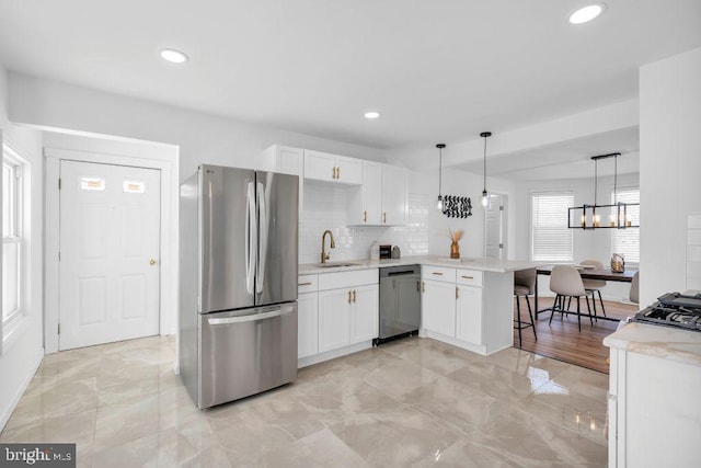 kitchen with appliances with stainless steel finishes, decorative light fixtures, white cabinetry, sink, and kitchen peninsula