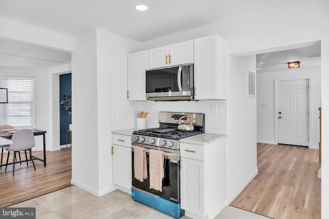 kitchen featuring light stone countertops, appliances with stainless steel finishes, white cabinetry, decorative backsplash, and light hardwood / wood-style flooring