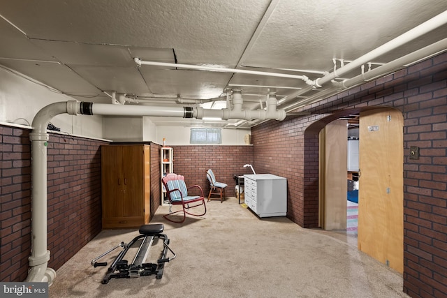 basement with brick wall, light carpet, and a textured ceiling