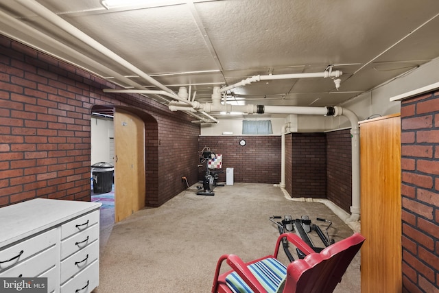 basement featuring brick wall, light carpet, and a textured ceiling