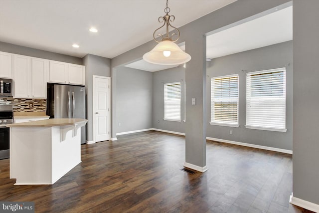 kitchen with pendant lighting, white cabinets, dark hardwood / wood-style flooring, backsplash, and stainless steel appliances